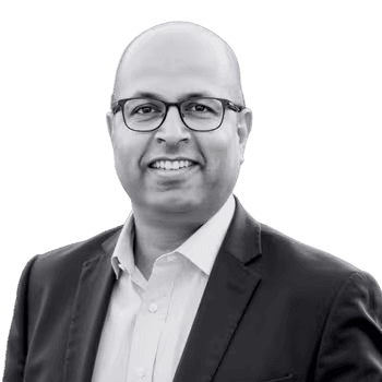 Black-and-white portrait of Rahul Todkar in glasses and a blazer, smiling.